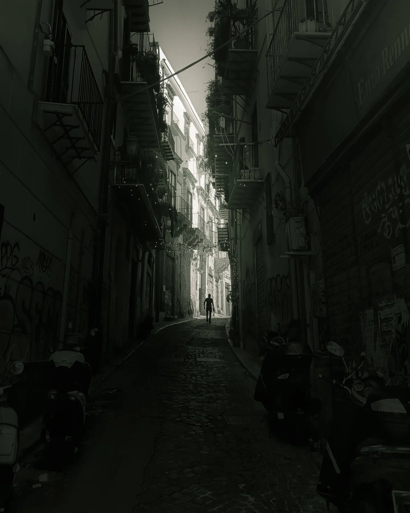 Deep narrow alley in shadow, a lone figure walking toward the bright opening at the far end