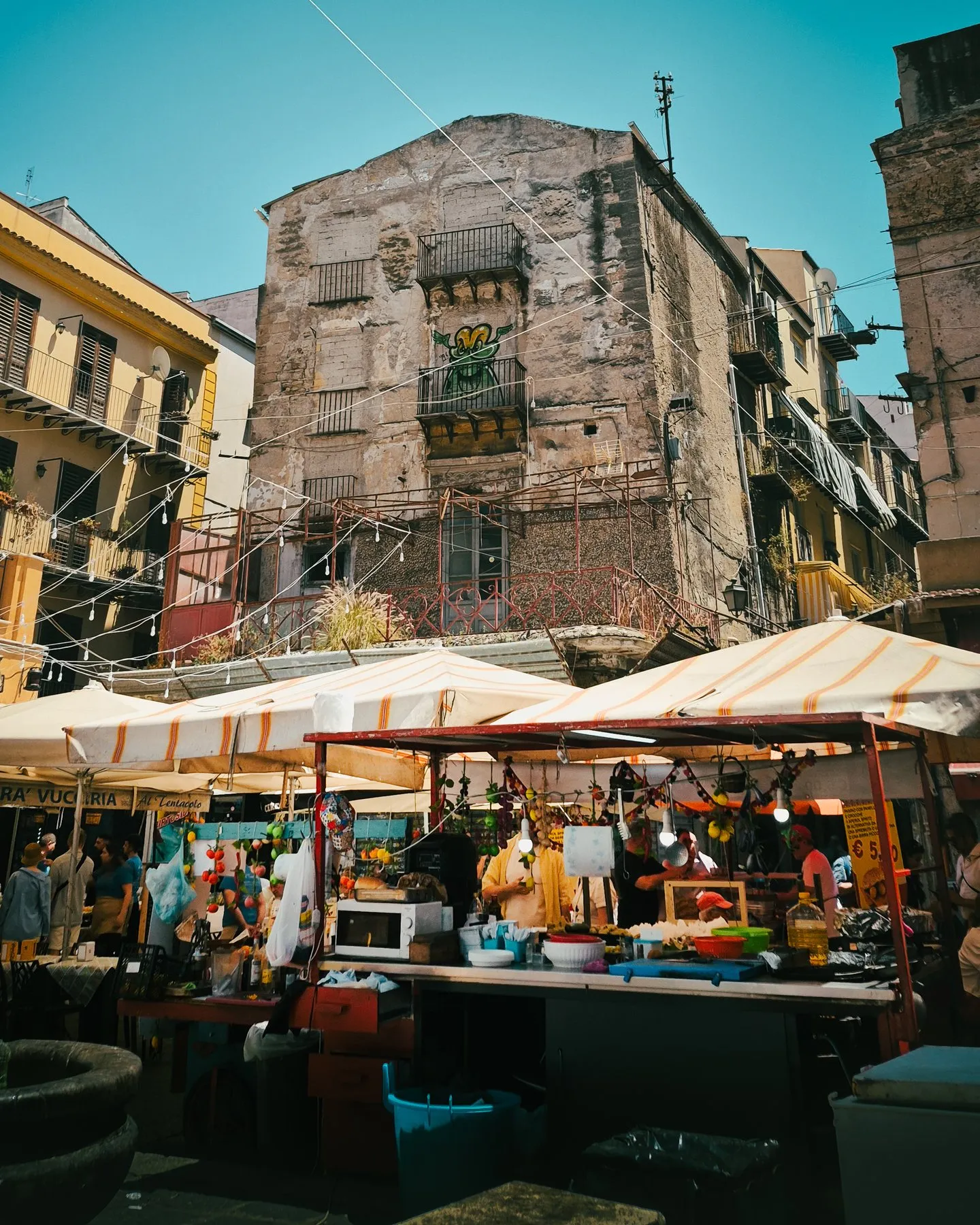 Street market stalls with striped awnings against a weathered stone building