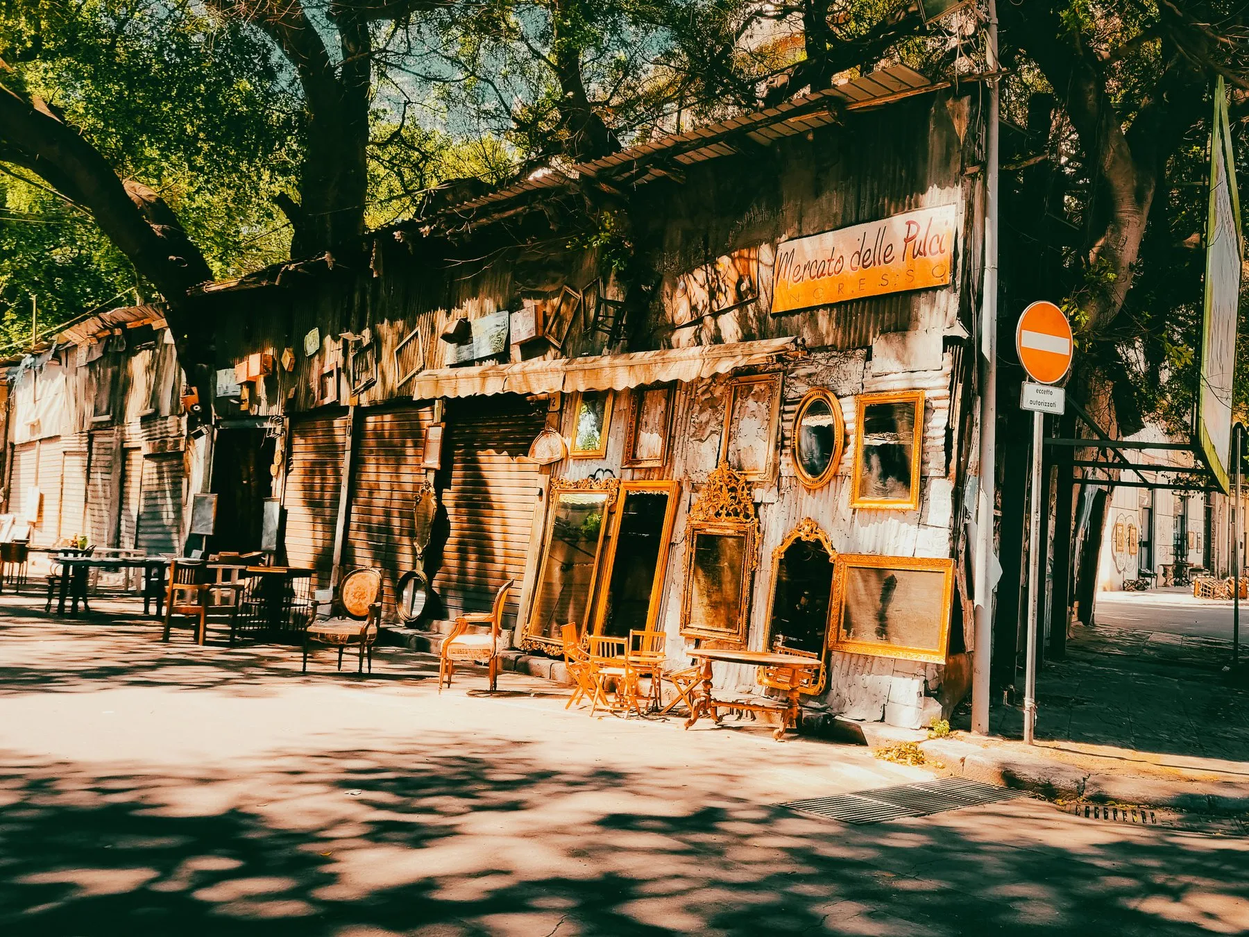 Antique stall displaying gilded mirrors and picture frames beneath plane trees