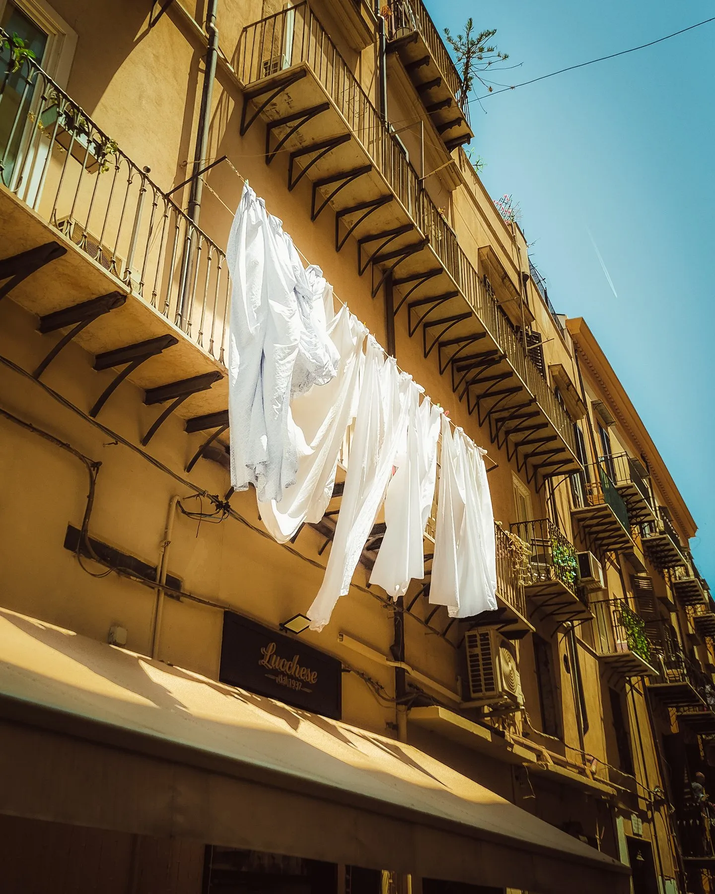 White sheets and shirts hanging from a balcony against a yellow facade