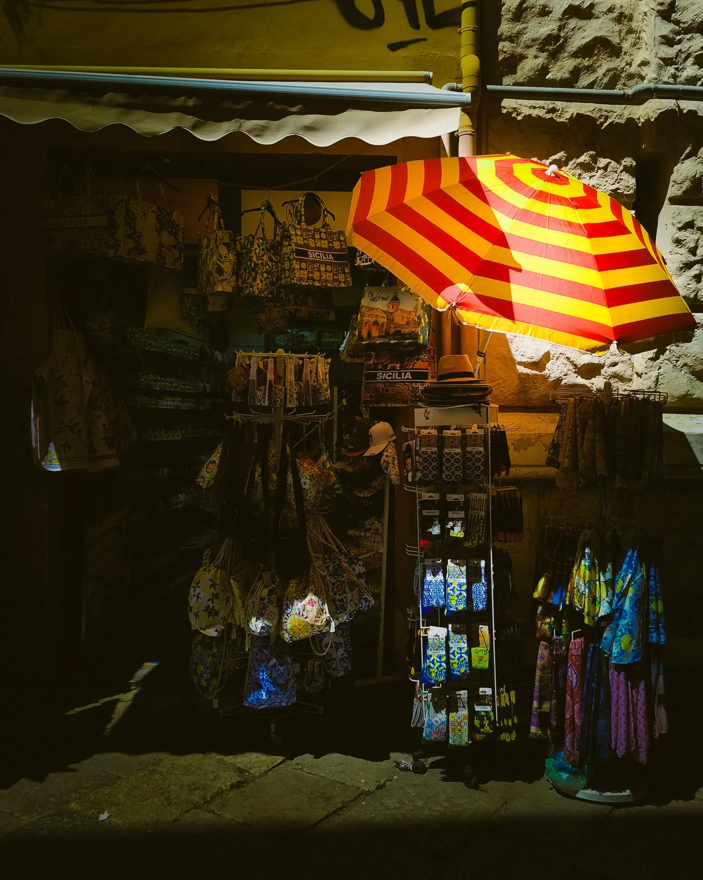 Souvenir stall with hanging garments under a red and yellow striped umbrella