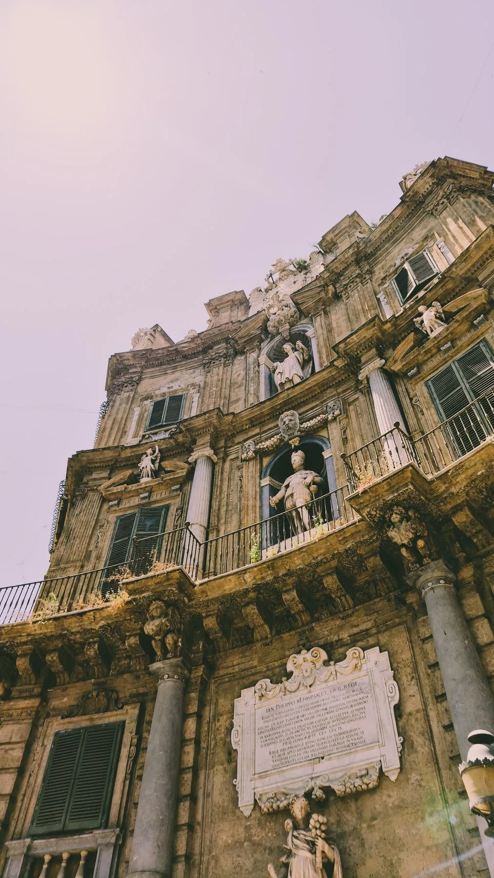 Baroque church facade crowned with stone statues under a pale pink sky